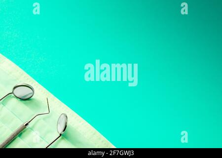 Dentist instruments: two mirrors and dental probe lying left on medical mask. On green gradient background. Stock Photo