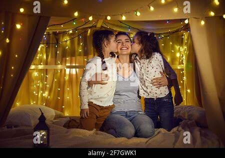 Happy daughters kissing loving mother in cheeks spend time in home tent Stock Photo