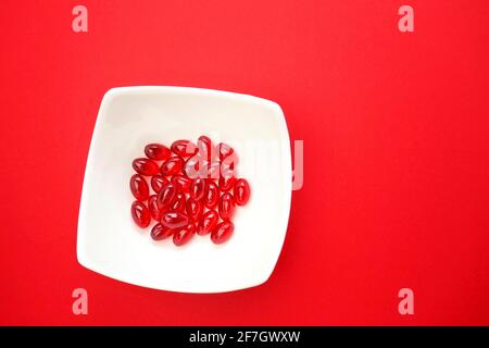 krill oil red gelatin capsules close-up.omega fatty acids.Natural supplements and vitamins.Red capsules with krill oil in a white ceramic cup on a