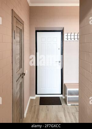 Hallway design in a small apartment with beige walls and brick texture. White front door, shoe cabinet, clothes hanger. Stock Photo