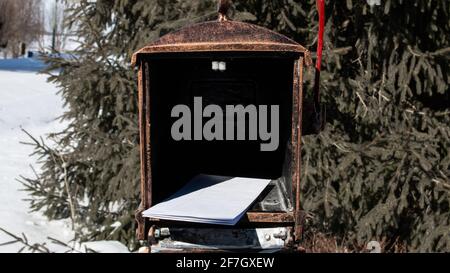 A stack of white legal envelops inside of a copper-tin mailbox in Ontario, Canada, evergreen spruce trees behind. February 2021. Stock Photo