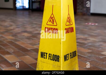 A dirty yellow four-sided wet floor sign on a dusty tile ground in London Ontario Canada, February 2021. Stock Photo