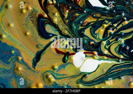 On the yellow liquid marble, blue and red streaks sprinkled with gold sparkles. Contemporary art. A colorful avant-garde painting with rich texture. A Stock Photo
