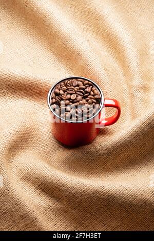 Red mug with coffee beans on twisted burlap background Stock Photo