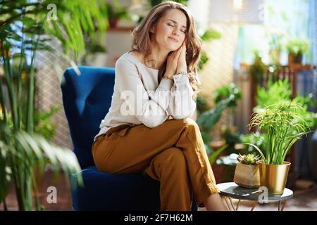 Green Home. relaxed trendy housewife with long wavy hair at modern home in sunny day in green pants and grey blouse sitting in a blue armchair. Stock Photo