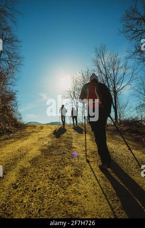 Group of people hiking or trekking on a fire road towards the sun. Sunny day, ideal for hiking, cold weather with sun in the background. Stock Photo