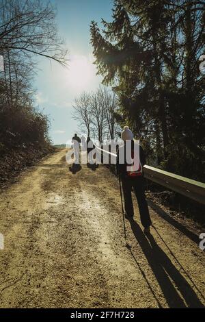 Group of people hiking or trekking on a fire road towards the sun. Sunny day, ideal for hiking, cold weather with sun in the background. Stock Photo