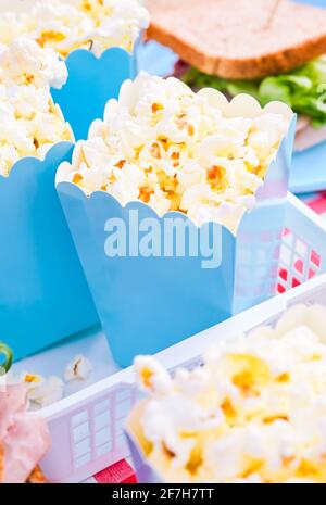 Popcorn and sandwiches for a snack outdoors in nature. in bright plastic dishes . Lunch in the park on the green grass. Summer sunny day and picnic basket. FullHD footage, Slow motion Stock Photo