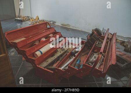 Open red tool box sitting on the ground of a construction site in an apartment. Tool box contains tools, screwdrivers, pliers, wrenches, tubes and so Stock Photo
