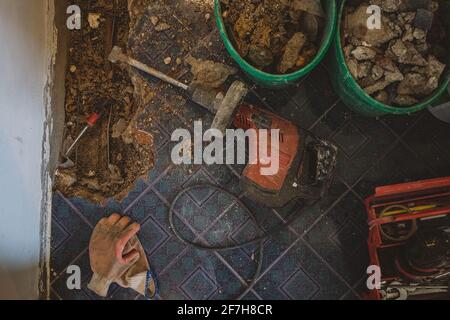 Red electric demolition hammer on the floor, while renovating an old water pipe in the ground. Construction site with tools, old material and gloves i Stock Photo