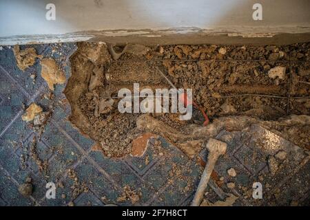Broken water pipe in an apartment. Visible hole in the ground with tiles, old concrete and debris. Construction site while trying to remedy a water le Stock Photo