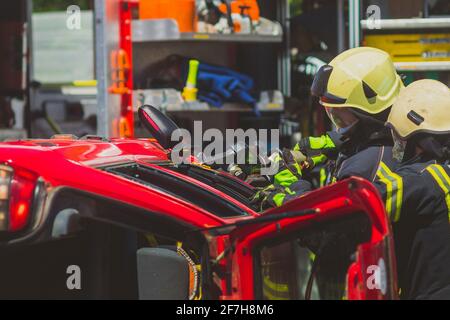 Firefighters using a hydraulic jaws of life or scissors to cut the crashed car open to save the driver caught inside. Emergency situation in a road cr Stock Photo