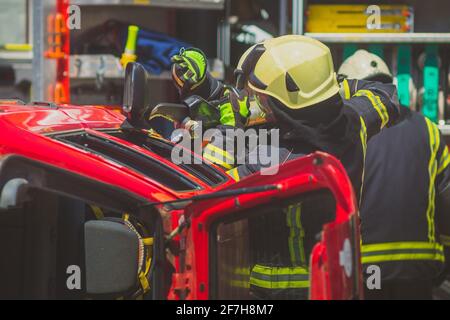 Firefighters using a hydraulic jaws of life or scissors to cut the crashed car open to save the driver caught inside. Emergency situation in a road cr Stock Photo