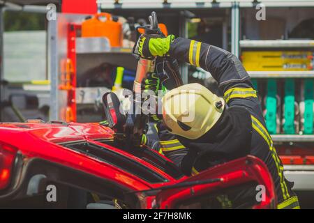 Firefighters using a hydraulic jaws of life or scissors to cut the crashed car open to save the driver caught inside. Emergency situation in a road cr Stock Photo