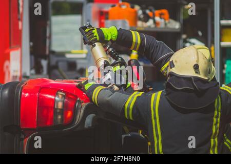 Firefighters using a hydraulic jaws of life or scissors to cut the crashed car open to save the driver caught inside. Emergency situation in a road cr Stock Photo