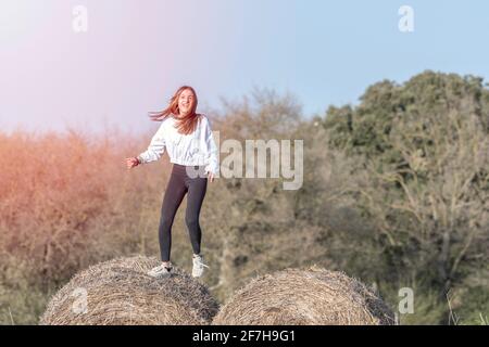 latina teenage girl in black leggings, top and jacket posing on straw bales  in rural setting, vertical, portrait Stock Photo - Alamy