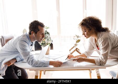 Concentrated business partners doing paperwork, learning financial graphs for making report. Stylish serious colleagues working on new strategy for Stock Photo