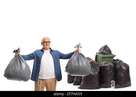 Full length portrait of a man holding two waste bags in front of a pile of bags and bin isolated on white background Stock Photo
