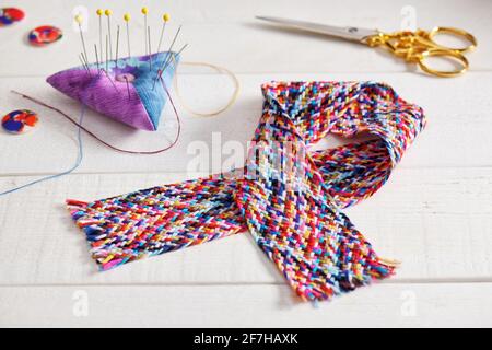 A braid of multi colored sewing threads, pincushion, scissors, buttons lying on a white surface Stock Photo