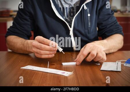 man in a jaket makes a rapid test for antibodies to coronavirus covid 19 at home. dropes a drop of analysis solution onto the rapid antigen test Stock Photo