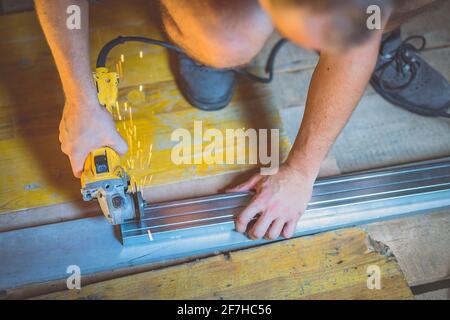 Photo of a person cutting holders, aluminium profiles or aluminium structural frames that hold drywall boards with an angle grinder in a house that is Stock Photo