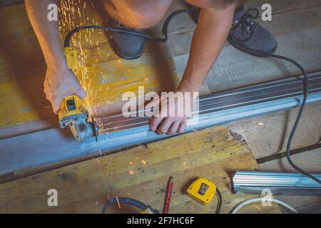 Photo of a person cutting holders, aluminium profiles or aluminium structural frames that hold drywall boards with an angle grinder in a house that is Stock Photo
