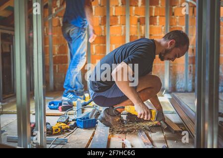 A person cutting holders, aluminium profiles or aluminium structural frames that hold drywall boards with an angle grinder in a house that is being re Stock Photo
