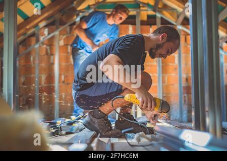 A person cutting holders, aluminium profiles or aluminium structural frames that hold drywall boards with an angle grinder in a house that is being re Stock Photo