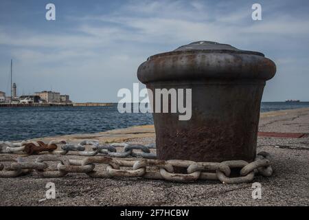 Old metal rusty mooring bollard with a chain wrapped around. Stock Photo