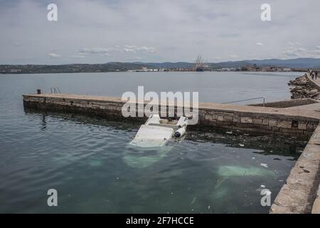 A small plastic boat partially sunk under water in a small marina close to a port of Koper in Slovenia. Debris or trash is seen floating in the water. Stock Photo