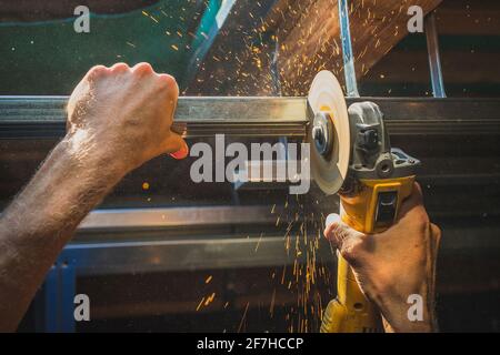 Photo of a person cutting holders, aluminium profiles or aluminium structural frames that hold drywall boards with an angle grinder in a house that is Stock Photo