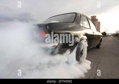 A black old vintage car is making a burnout on an empty street. Smoking and burning tires on a back road. Stock Photo
