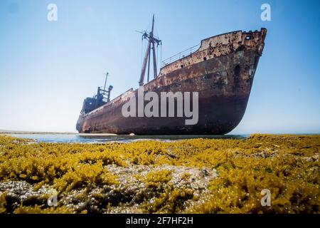 Dimitrios shipwreck in  Gythio, Greece. A partially sunk rusty metal shipwreck decaying through time on a sandy beach on a sunny day. Famous shipwreck Stock Photo