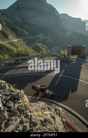 Motorcyclist driving and leaning into a curve on a famous albanian mountain road SH20, full of hairpins and tight turns at early evening. Stock Photo