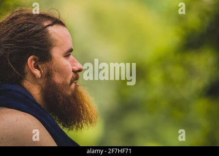 Side portrait of a hipster looking man with a long beard and hair, looking forward in the distance. Background in smooth bokeh out of focus, with plen Stock Photo