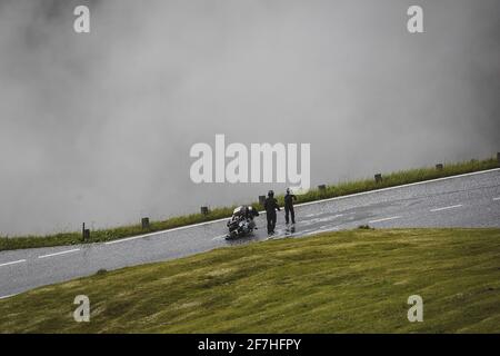 A couple standing next to a crashed motorcycle due to a slide on a very slippery road covered with ice and snow on a high mountain pass.  Dangerous co Stock Photo