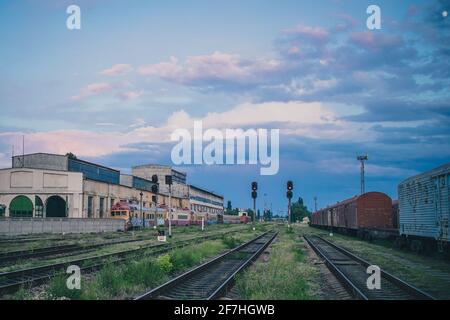 Far side of train station in Chisinau, Moldova on a summer evening. Signals ar shining red, with some old trains and wagons in the background. Stock Photo