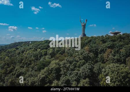 Motherland monument in Kiev poking out of the forest on a sunny day with blue skies. Majestic photo of a big statue on the hill in Kvyv, Ukraine Stock Photo