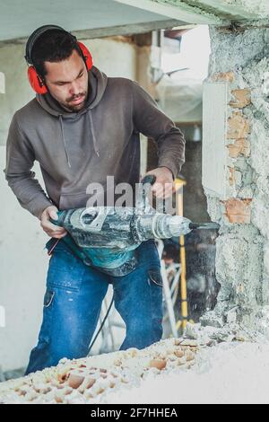 A person using an automatic hammer demolishing a house wall during a reconstrucion. Stock Photo