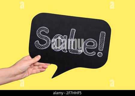Female hand holds a sign with the inscription 'Sale' on a yellow background. Stock Photo