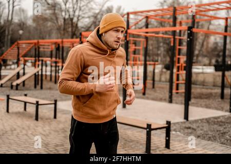 Young man in sports outfit doing morning workout outdoors. Young man running on street sports ground. Staying fit and healthy concept Stock Photo