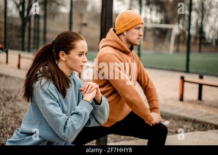 Young couple in sports outfit doing morning workout outdoors. Young man and woman stretching they muscle before running on street sports ground Stock Photo