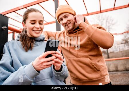 Young attractive sport woman and man in sportswear are smiling and she is holding phone at sports park Stock Photo