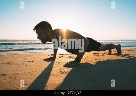 Young fit man doing push ups or exercising on the beach during sunrise  Stock Photo