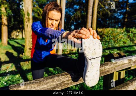 Young woman beautiful adult stretching her hamstrings touching her toes in a wooded park at sunset point concept sport weekend afterwork Stock Photo