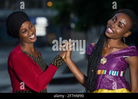 Young women standing outdoors laughing at each other. Stock Photo