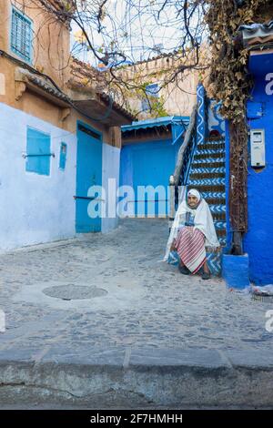 Chefchaouen, Morocco - November 4, 2018: Moroccan elderly woman sitting on a stairs. Stock Photo