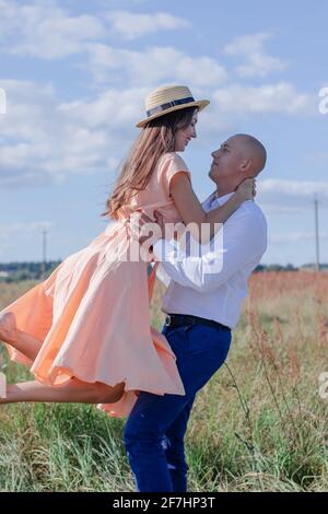 happy couple dancing in the field. brunette in cream dress and bald man in white shirt and blue pants. husband and wife on a romantic date. love story Stock Photo