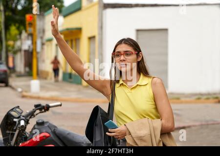 Latin Businesswoman with smart phone hailing taxi on city street. Stock Photo