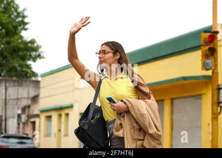 Latin Businesswoman with smart phone hailing taxi on city street. Stock Photo